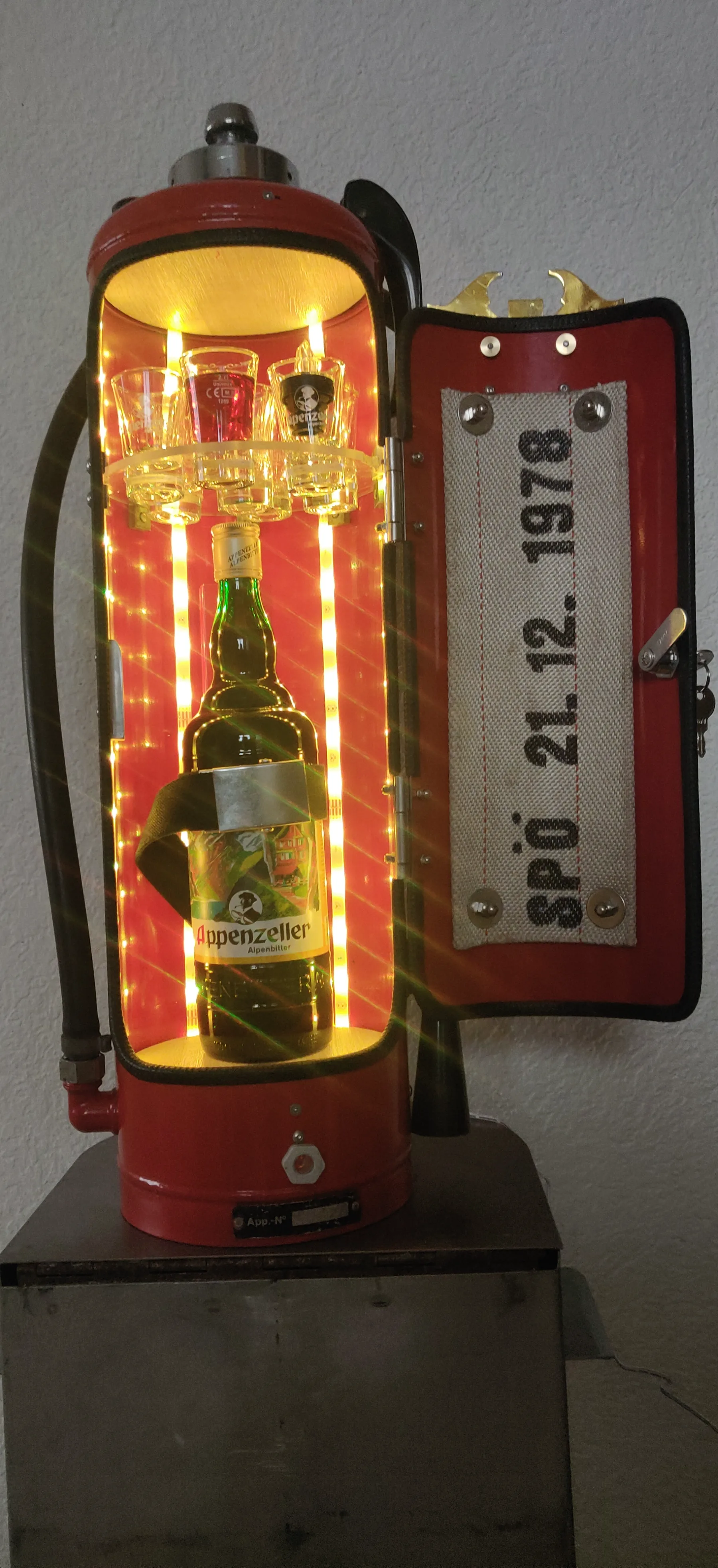 Rote Mini-Bar mit Appenzeller-Flasche, Shot-Gläsern und Feuerwehrschlauch-Applikation in der Türe