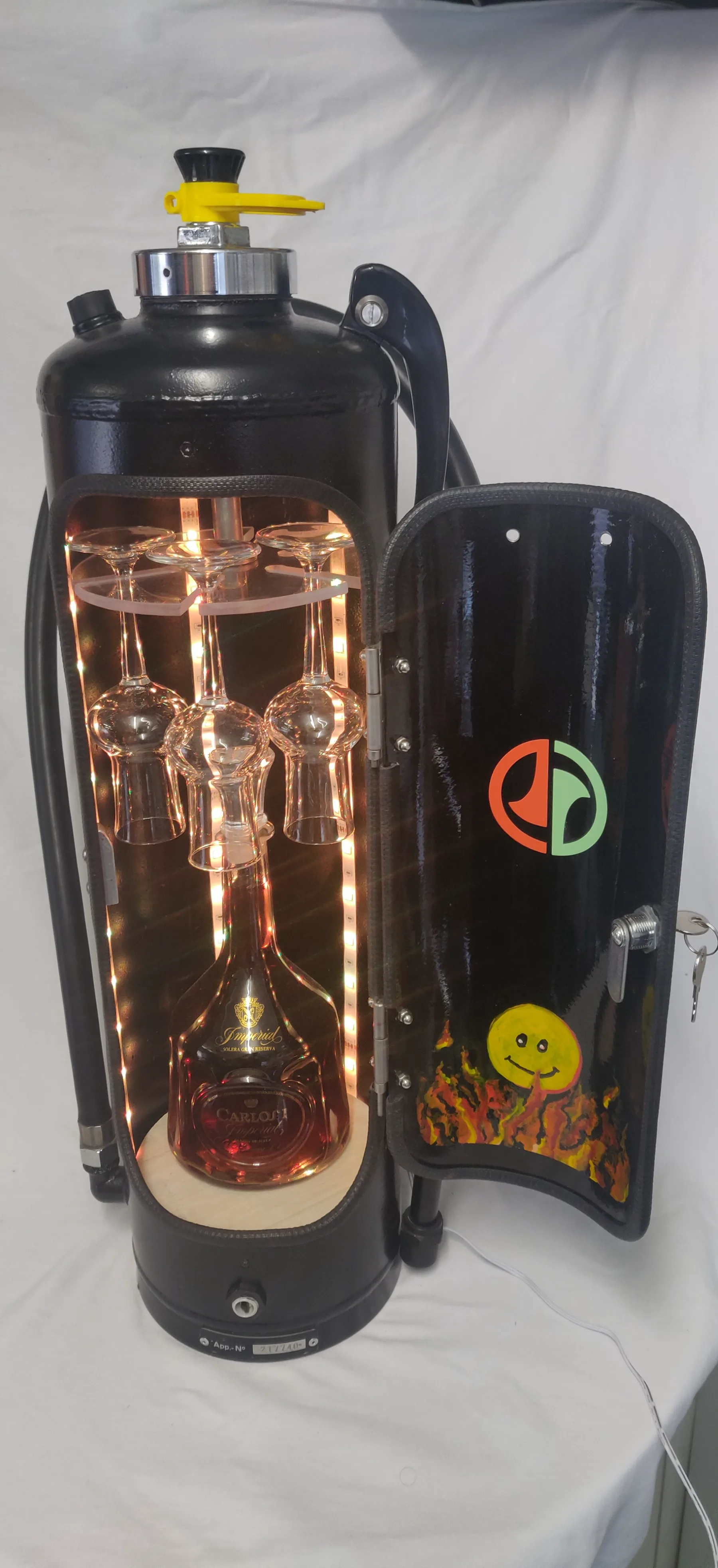 Feuerlöscher umgebaut zur Mini-Bar mit hängenden Gläsern und Karaffe, warm beleuchtet