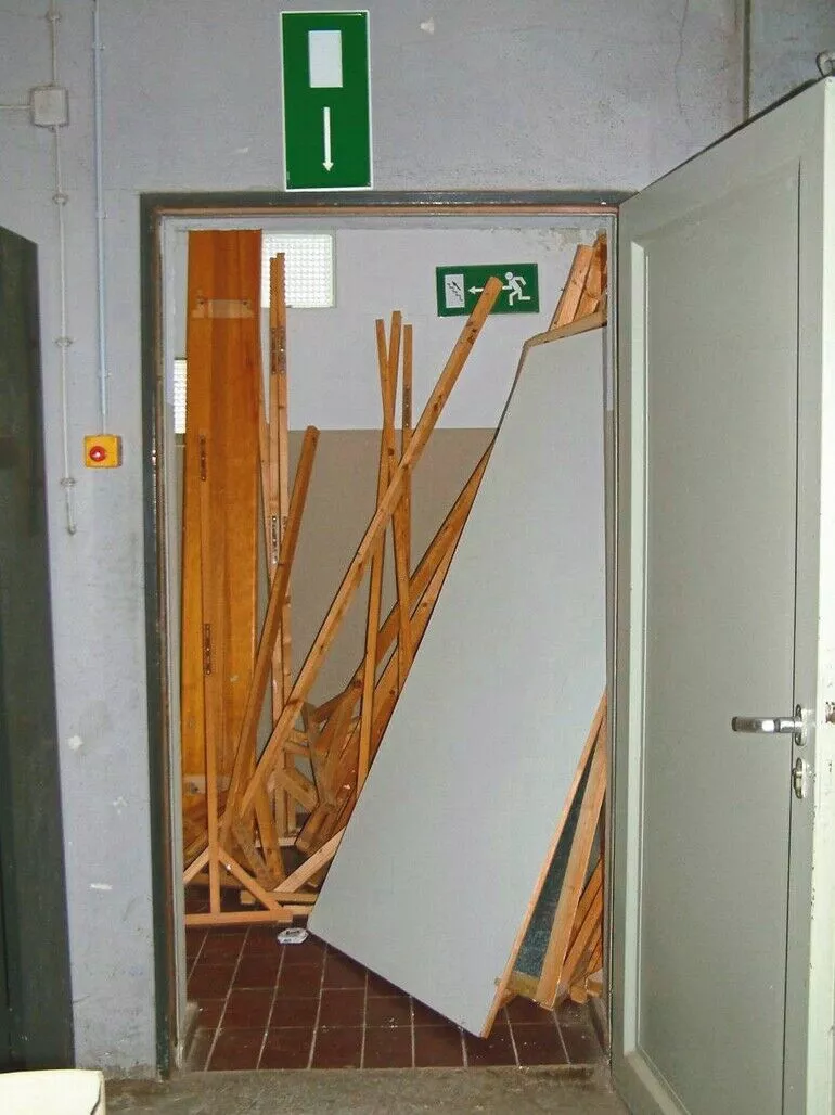 Durch Holzlatten und Platten verstellter Fluchtweg trotz Rettungszeichen