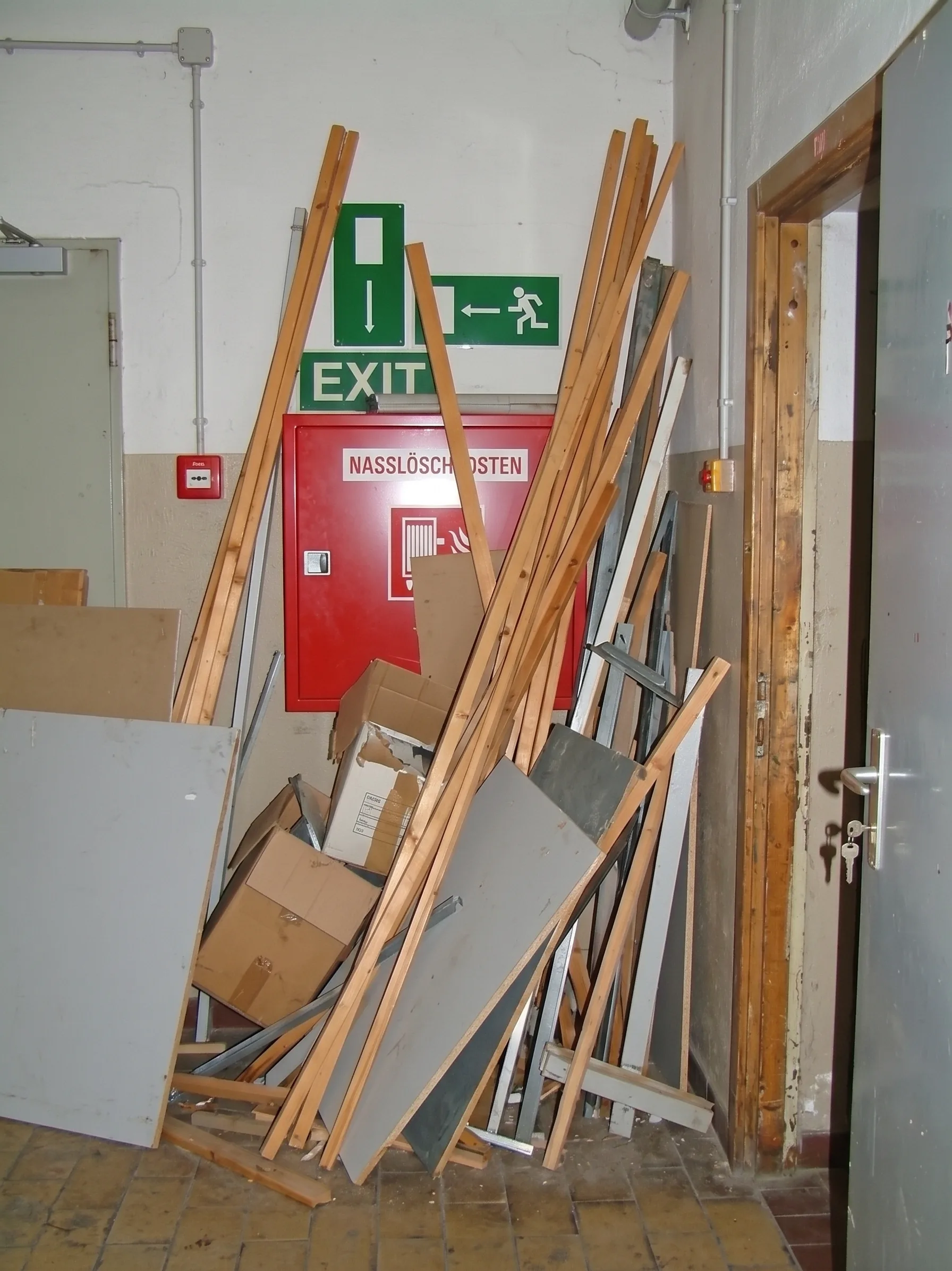 Nasslöschposten und Exit-Schild durch angelehnte Holzlatten und Platten verdeckt
